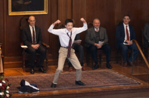 Boy in a suit showing muscles in front of teachers